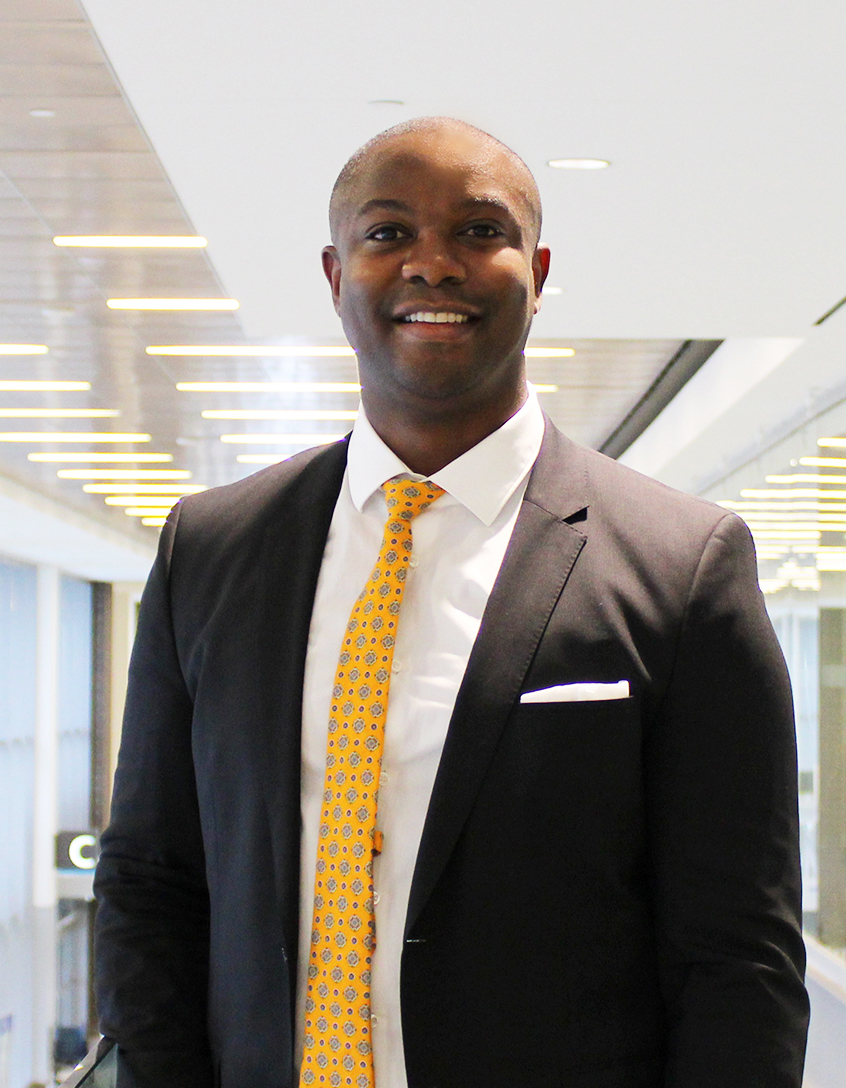 Dr. Ayeni stands in a bright hallway at Humber River Hospital, wearing a suit jacket and a yellow tie