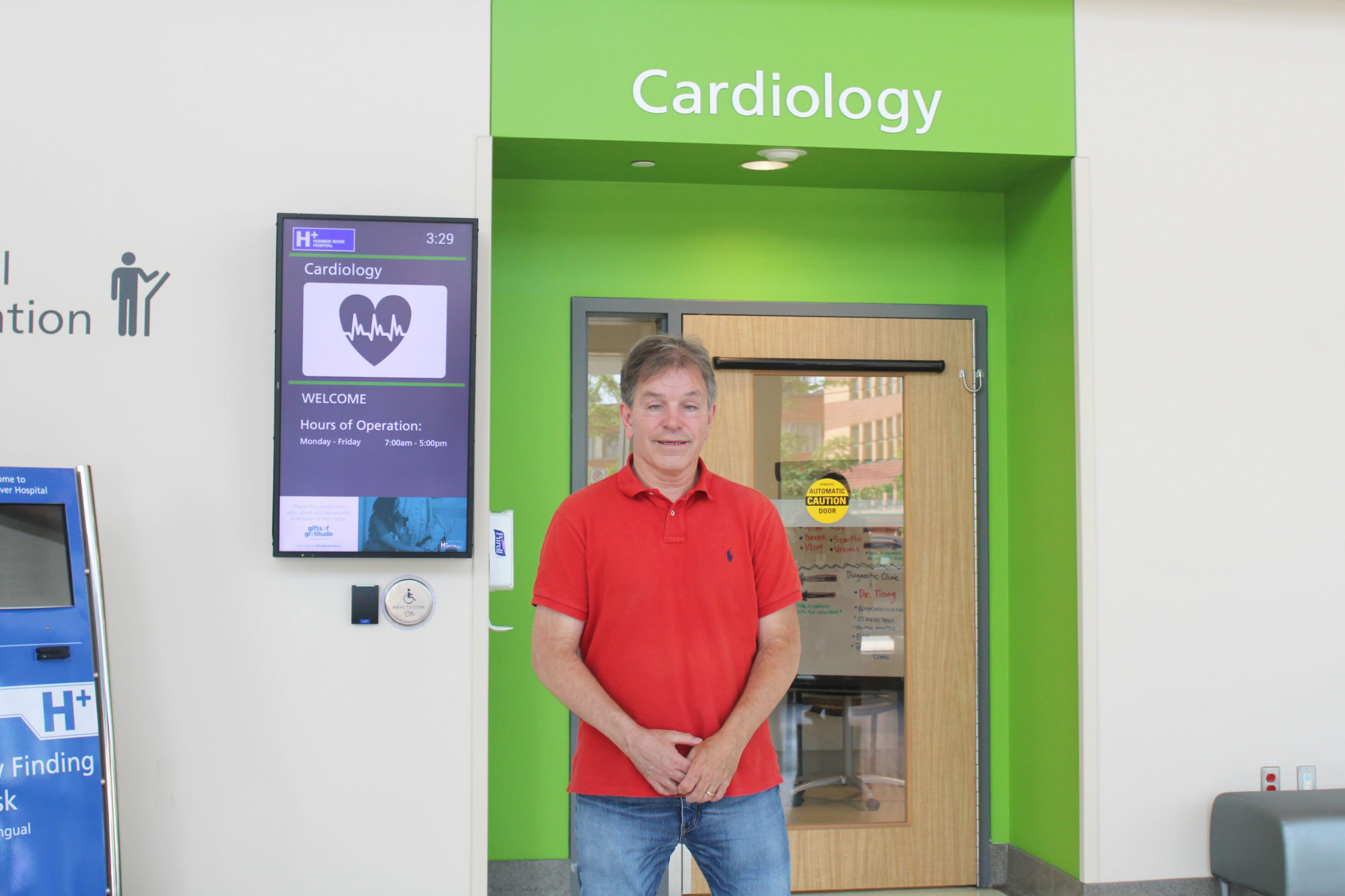 Jeff stands in front of the Cardiology Clinic, looking at the camera with his hands clasped in front of him.