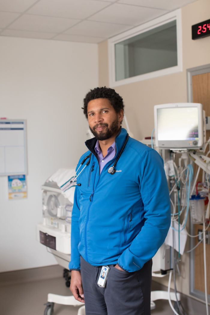 Dr. Graham Black stands in a NICU room looking at the camera. An incubator is behind him.