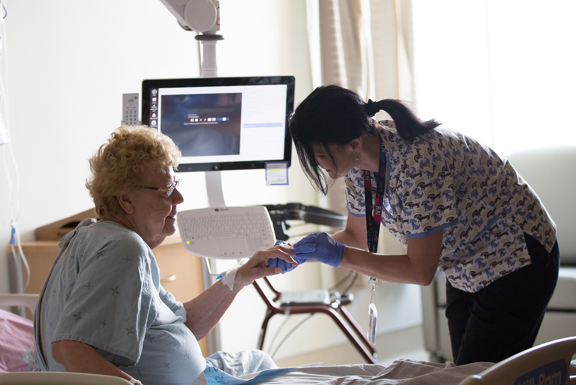A nurse checks a senior patient's finger in her inpatient room