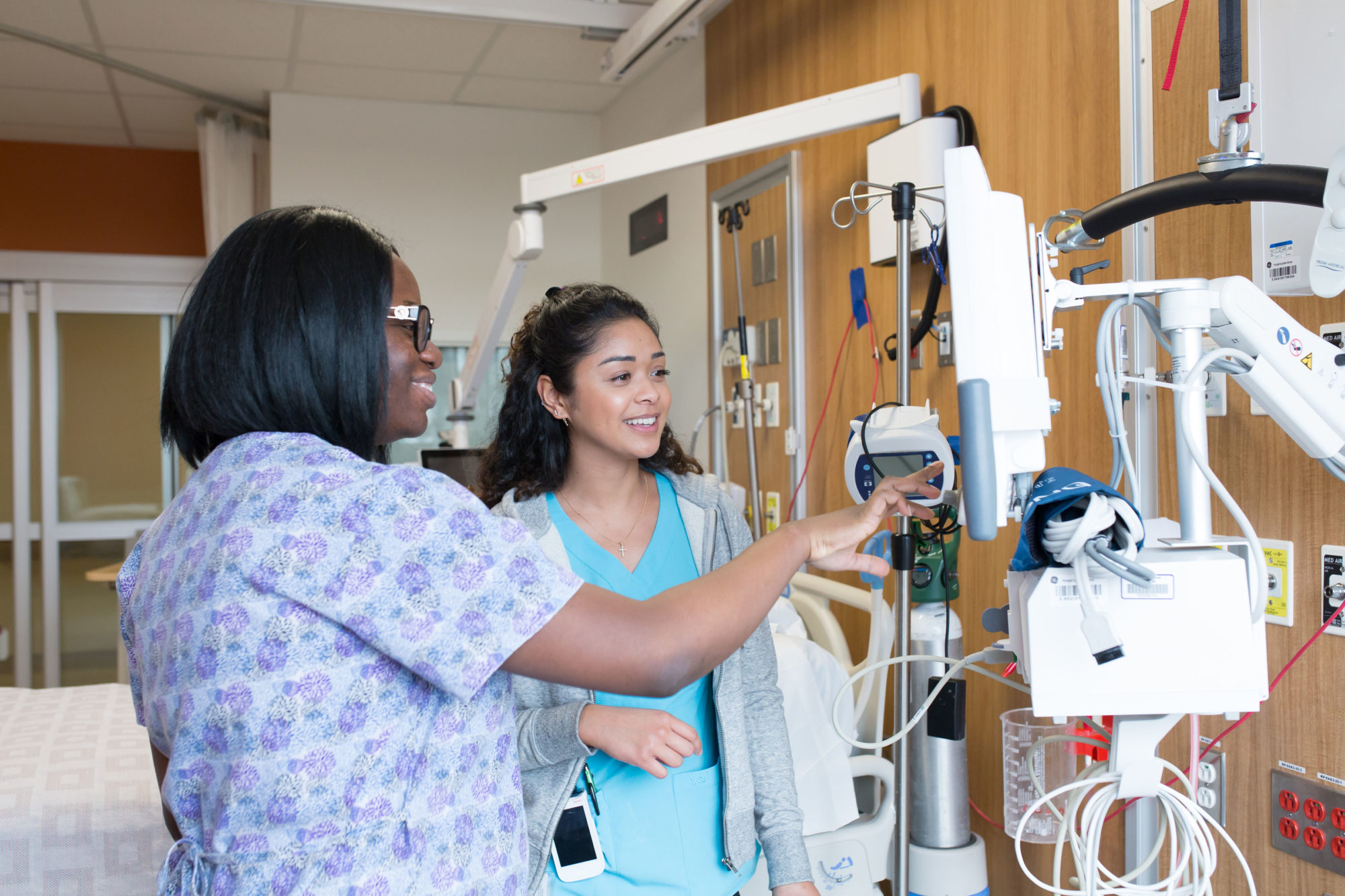 Two female nurses in our ICU stand in an empty inpatient room setting up equipment.