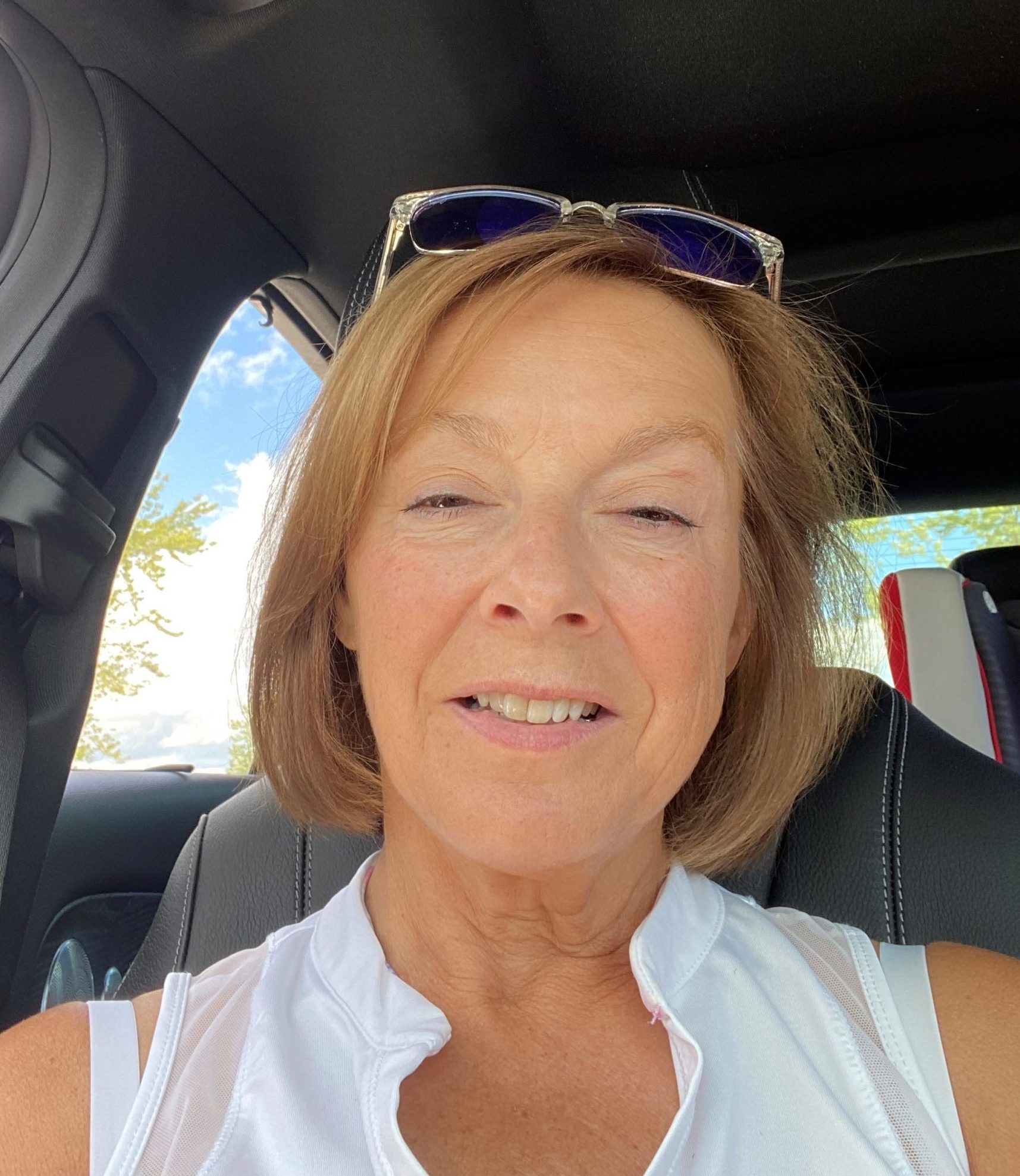 Michelle in her car taking a selfie. She has sunglasses on top of her head and is smiling into the camera.